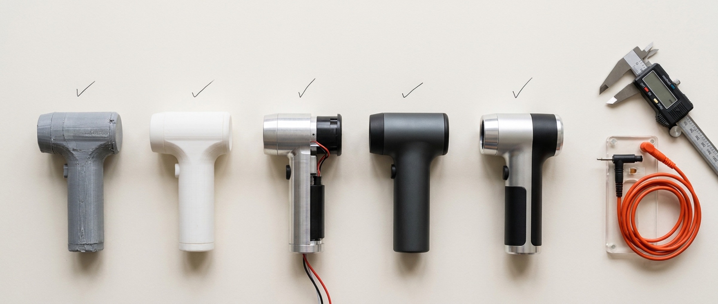 Five prototype iterations of a handheld device lined up beside calipers and an orange test lead